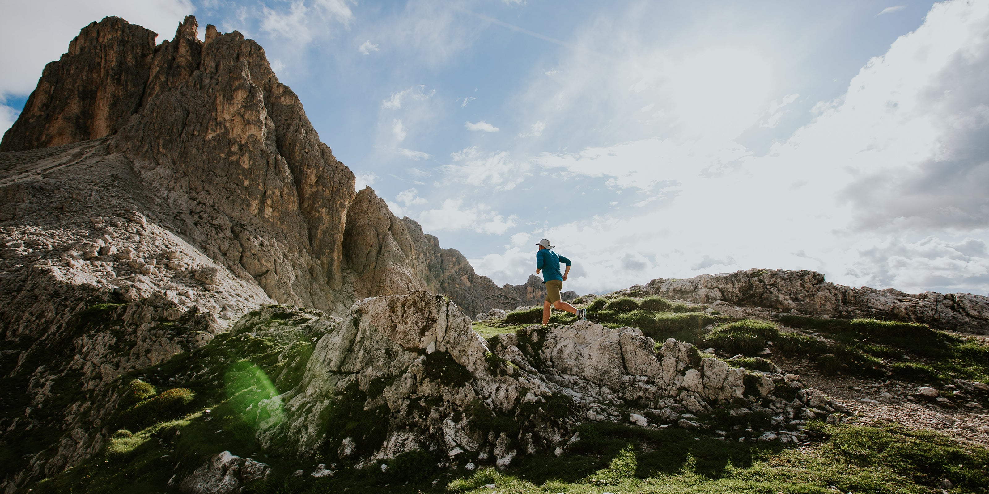 A picture of a man running up a trail to a mountain peak with blue skies in the background.