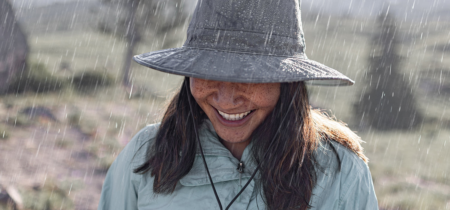 A woman wearing a Sunday Afternoons rain hat with rain pouring down.